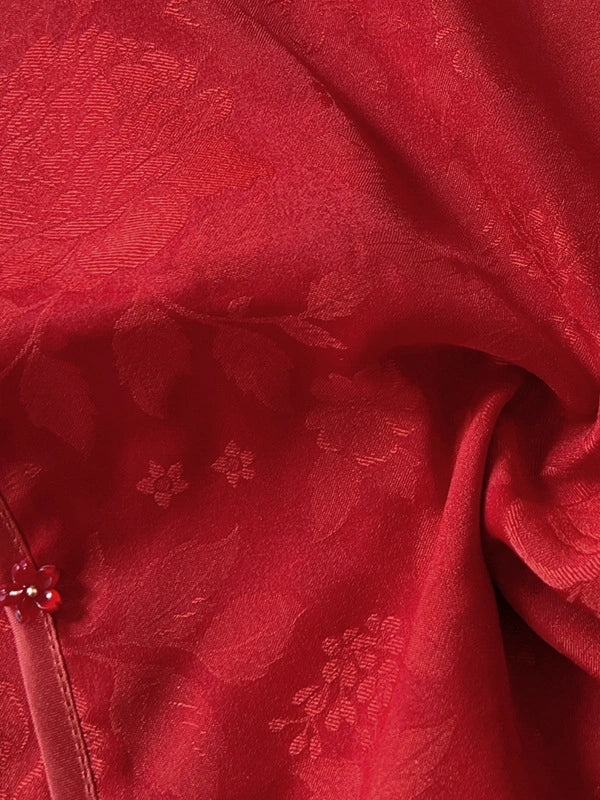 A close-up of red fabric with a subtle floral jacquard pattern and soft draped folds.