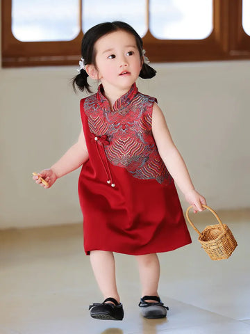 Child wearing a red Girls' "Good Fortune" Traditional Sleeveless A-Line Jacquard Qipao dress with intricate patterns, holding a small basket indoors.