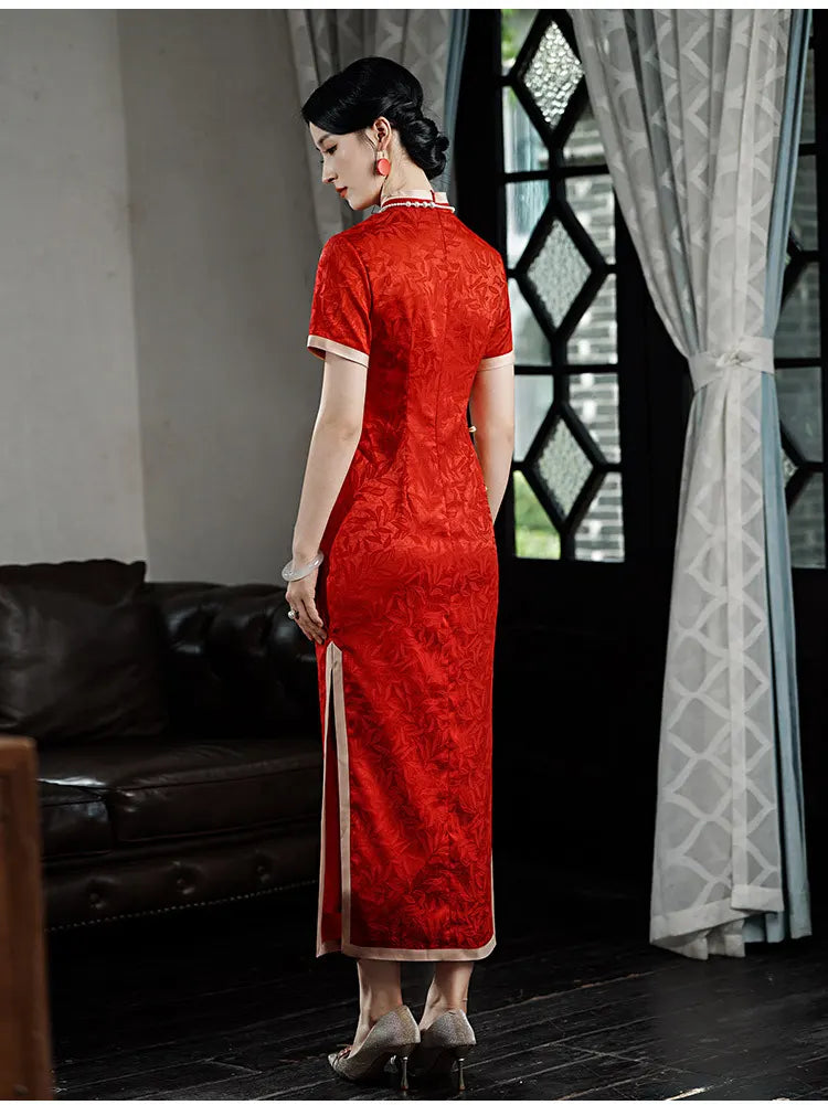 Woman in aRed & Gold Foral Jacquard Qipao - Chinese Wedding Tea Ceremony Dress  standing in a room with a couch and window.