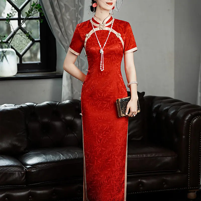 Woman in a Red & Gold Foral Jacquard Qipao - Chinese Wedding Tea Ceremony Dress sitting on a black leather couch.