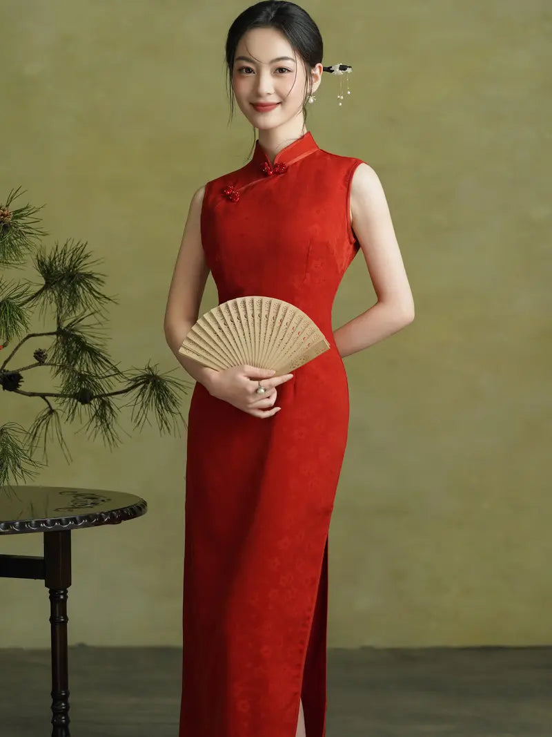 A woman wearing a sleeveless red cheongsam/qipao dress stands against a muted olive background, holding a light beige folding fan. A small table and pine branch appear at the left edge.