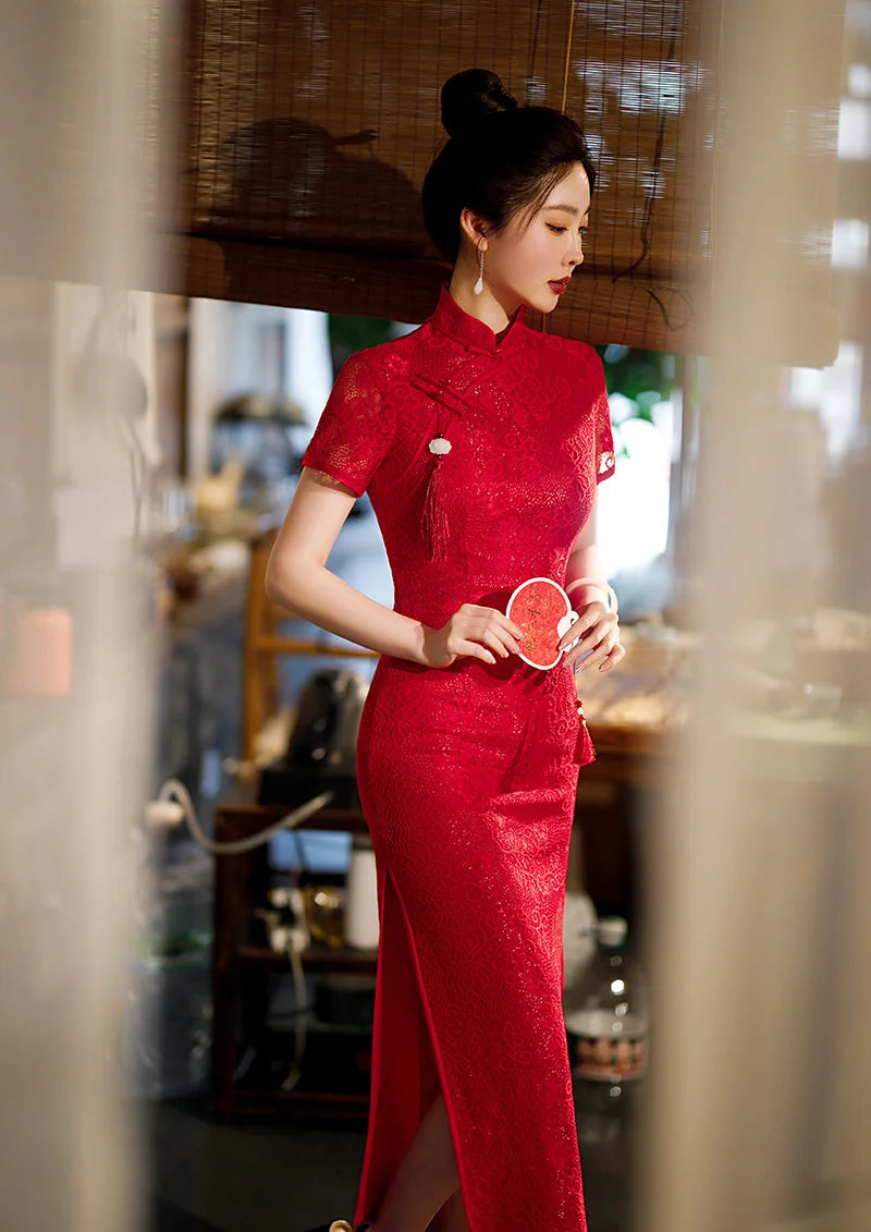 Woman in a traditional Red Lace Midi Length Short Sleeves Qipao Dress  outfit holding a red flower in a blurred indoor setting