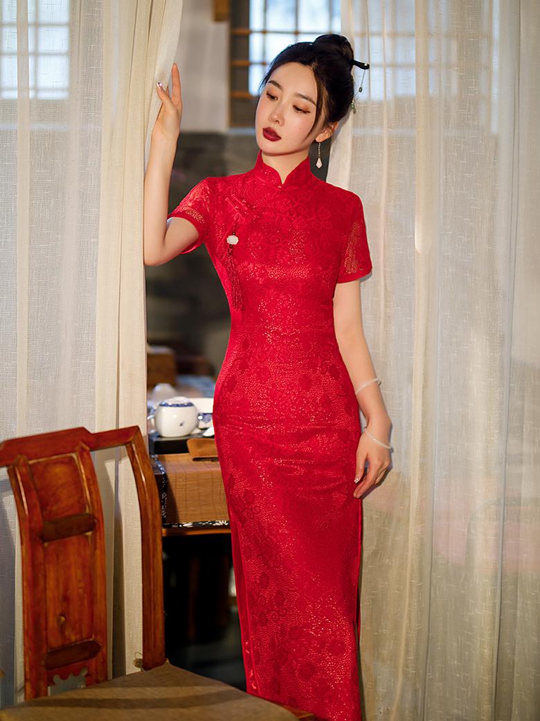 Woman in aRed Lace Midi Length Short Sleeves Qipao Dress standing in a room with curtains and wooden furniture.
