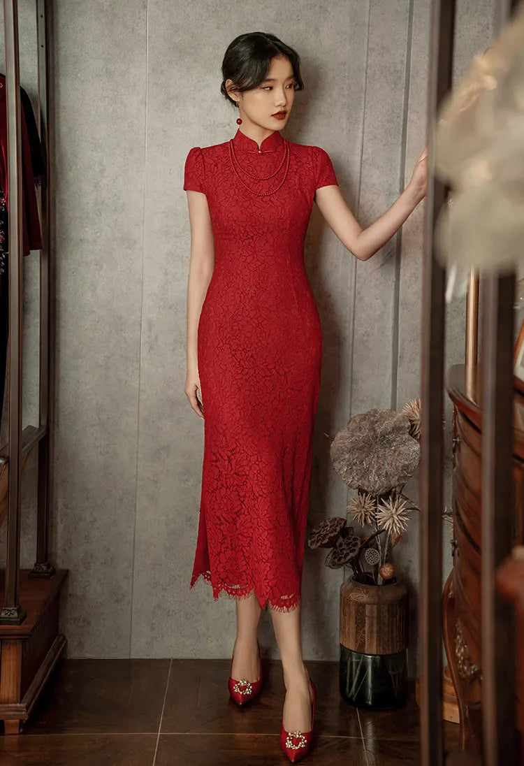 Woman in a Red Lace Open Back Cheongsam Wedding Dress standing in a room with a neutral wall and wooden furniture.