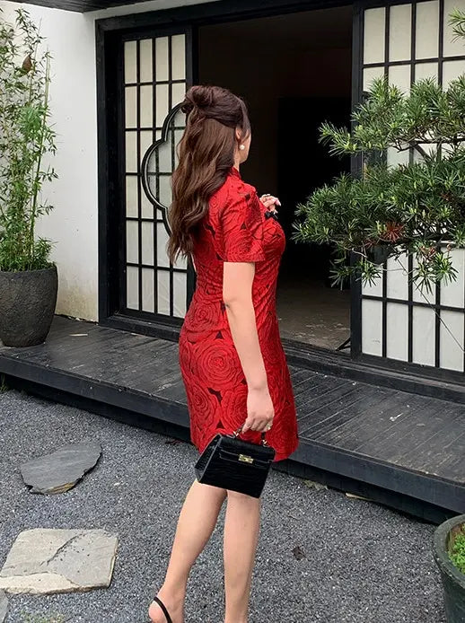 Woman in a Red Plus Size Modern Rose Jacquard Qipao  dress standing outside a building with plants around.