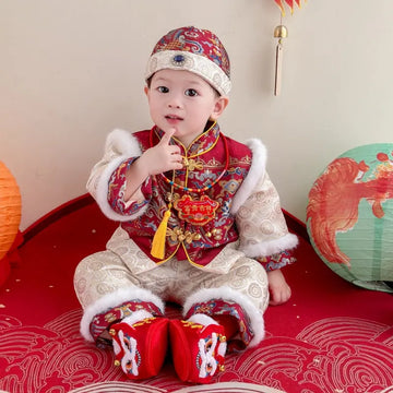 Child in traditional Chinese Red Quilted  Baby Winter Tang Suit Set outfit with decorative hat and shoes, sitting on a red surface.