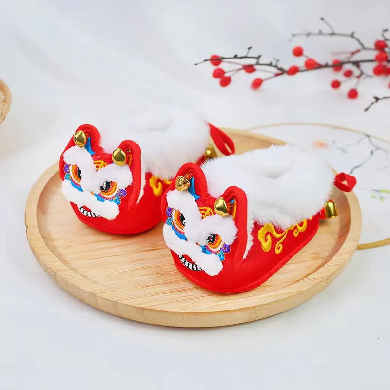 Red and white babay lion dance shoes on a wooden tray with a decorative background