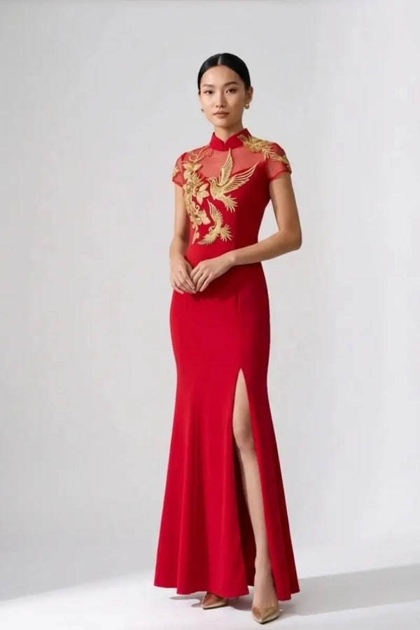 A woman modeling a red floor-length dress with gold embroidered phoenix motifs on the bodice and sleeves, photographed against a plain light gray studio background.