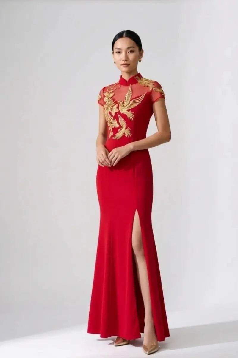 A woman modeling a red floor-length dress with gold embroidered phoenix motifs on the bodice and sleeves, photographed against a plain light gray studio background.