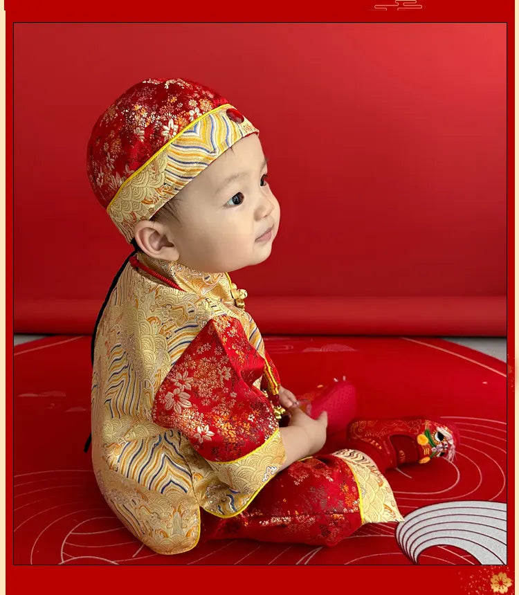 Baby in traditional Chinese outfit sitting on a red surface with a red background