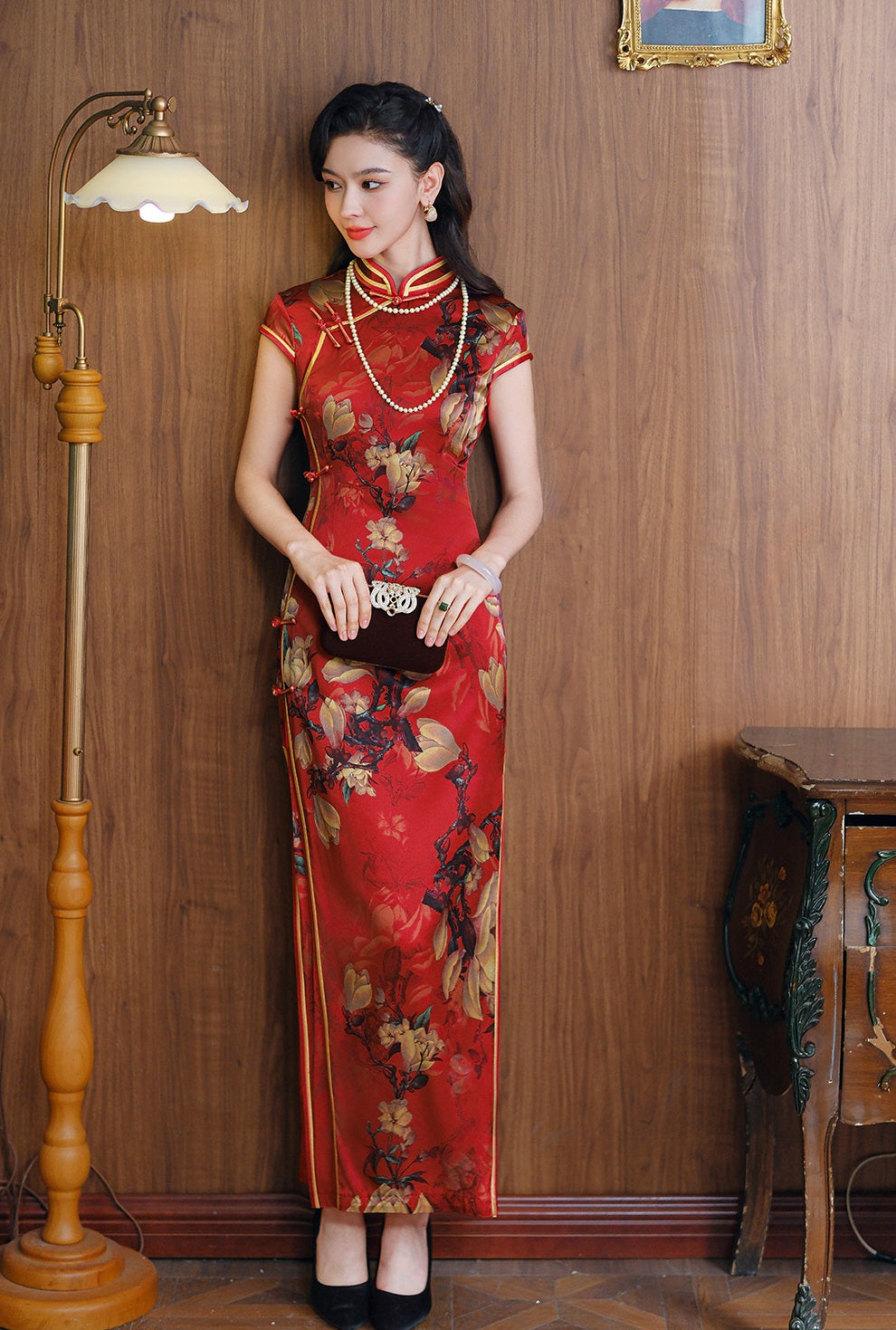 a chinese girl in red long floral silk qipao next to a lamp
