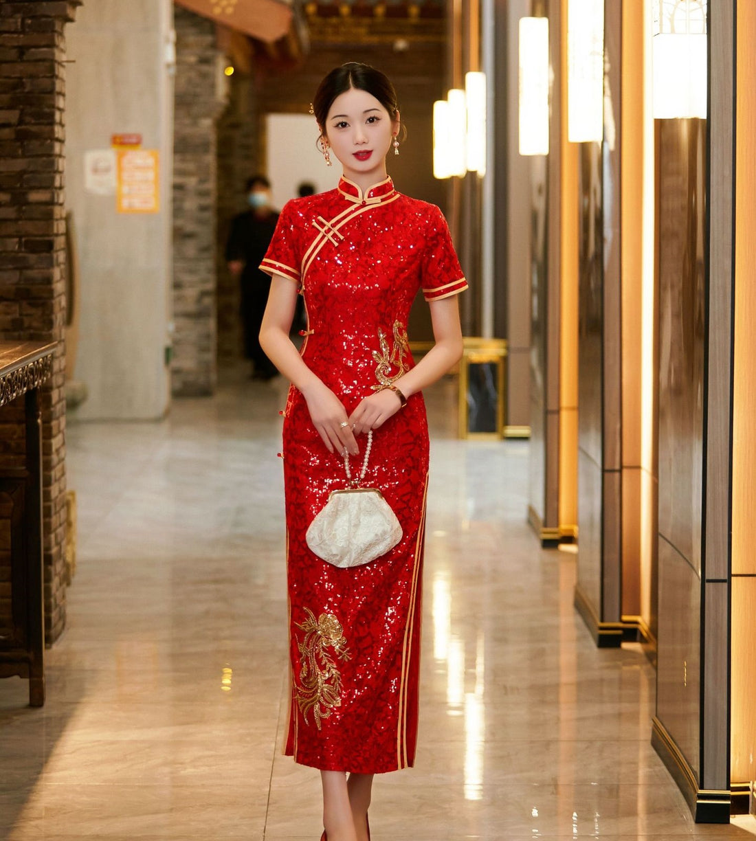 A woman wearing a red sequin qipao wedding dress with gold flower, featuring a high mandarin collar and a fitted silhouette. She holds a white satin clutch and is standing in a well-lit, elegant hallway, looking down