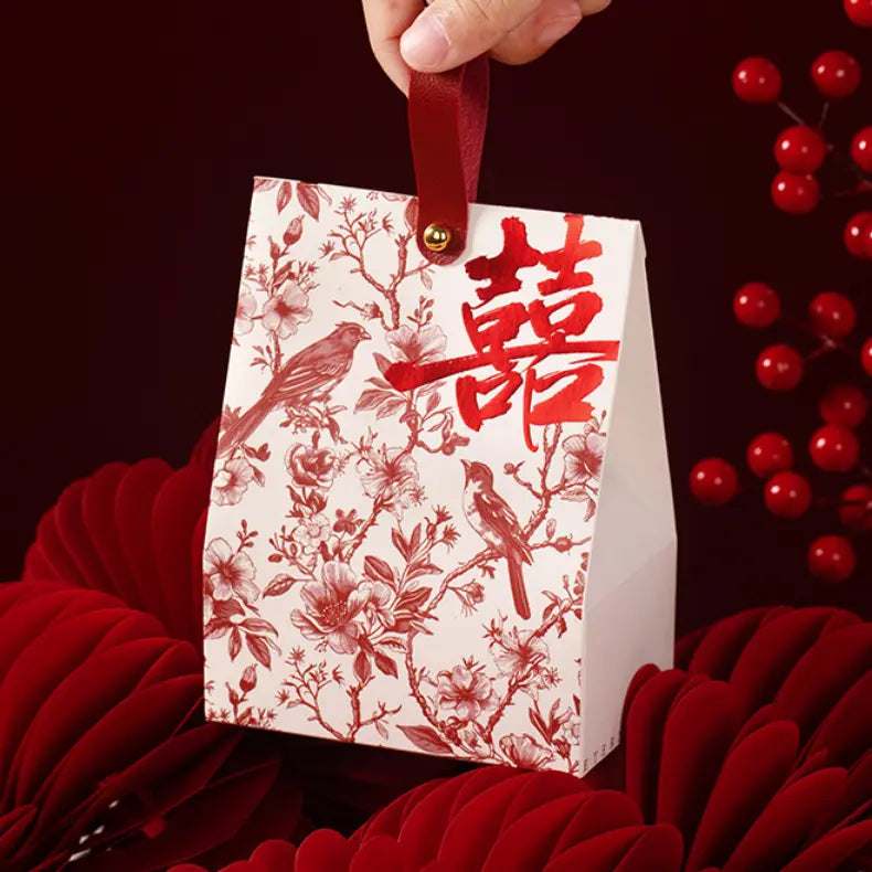 Gift bag with red floral patterns and Chinese double happiness characters, held by a hand against a dark background with red berries.