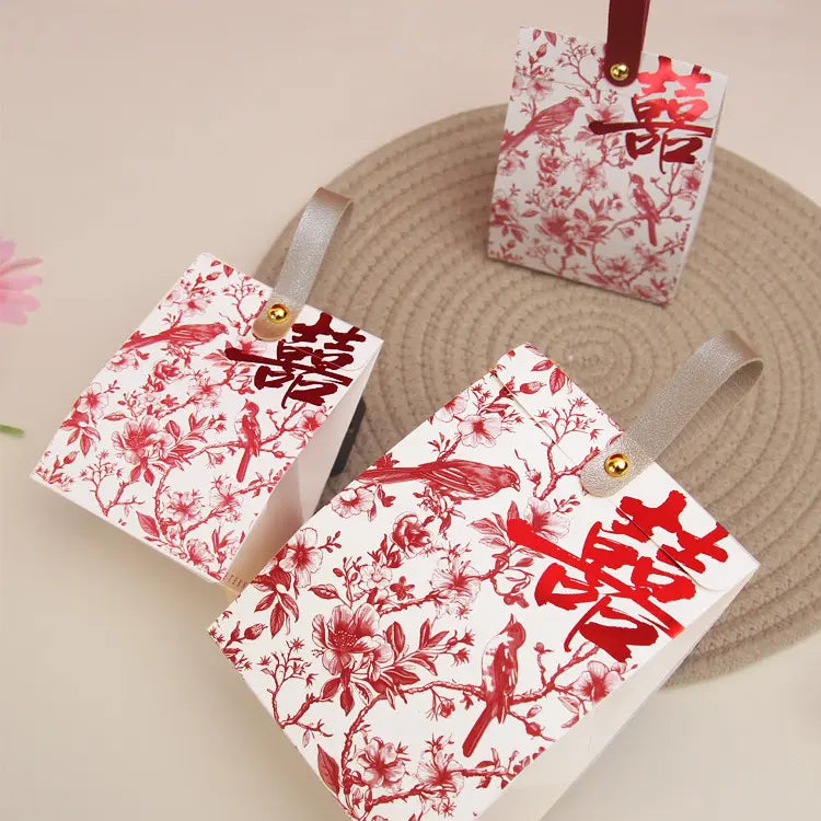 Three red and white Retro Chinoiserie Bird & Floral Wedding Candy Gift Boxes with bird designs on a beige surface.