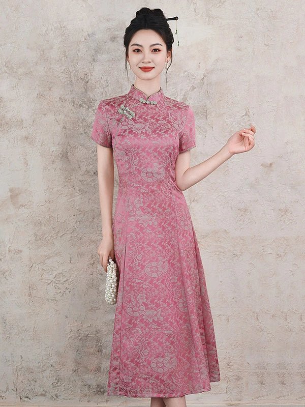 A woman wearing a pink short-sleeve cheongsam dress with a subtle floral pattern, standing against a textured beige wall and holding a small pearl clutch.
