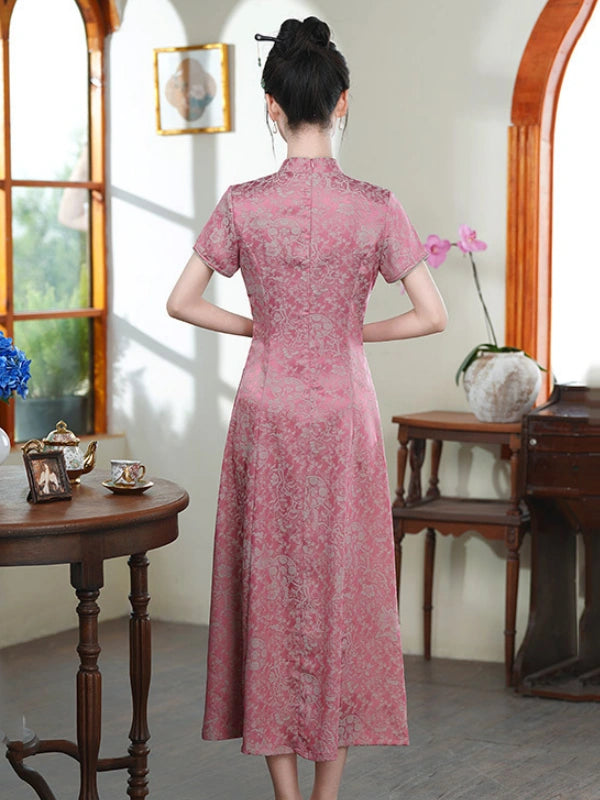 A woman viewed from behind wearing a pink short-sleeved midi qipao cheongsam dress with a subtle tonal floral jacquard pattern, standing in a vintage-style room with wooden furniture and arched windows.