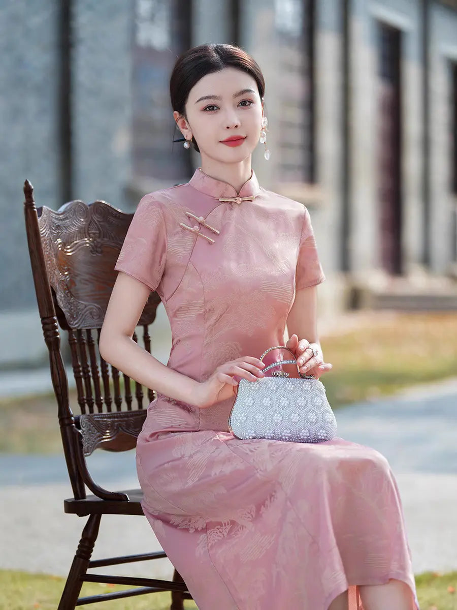 A woman wearing a  short-sleeve  Rose Pink Landscape Jacquard Modern A Line Qipao cheongsam dress sits on a dark wooden chair outdoors, holding a light blue patterned handbag.