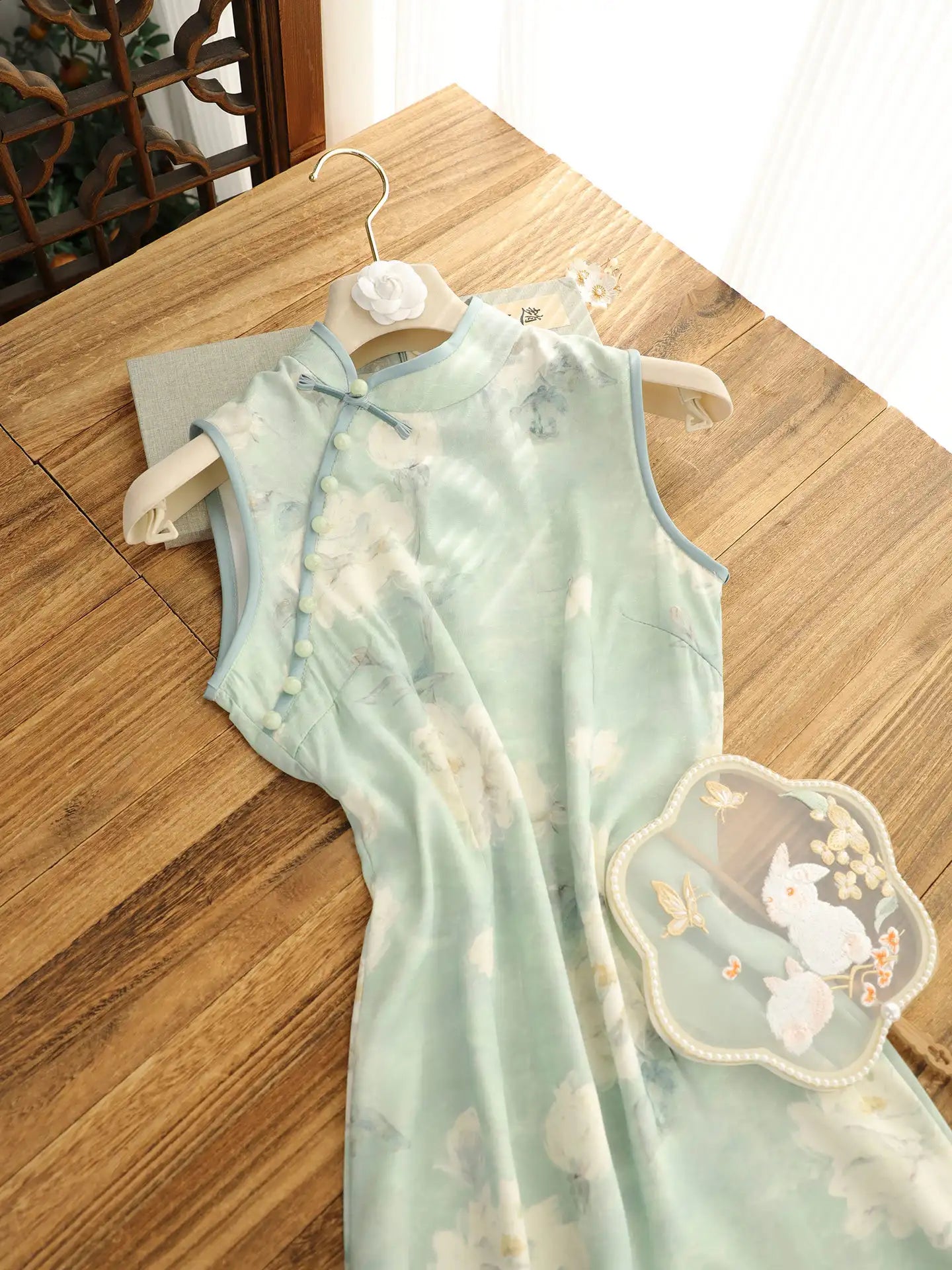 Sage Green Floral Neo-Chinese Sleeveless Qipao Dress  with floral embroidery on a wooden table