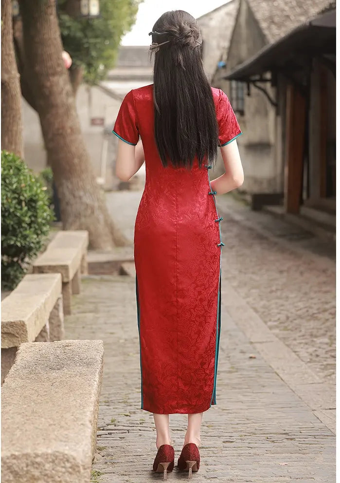 Woman in a red traditional Short Sleeves Floral Jacquard Long cheongsam Dress With Blue Trim walking away on a stone path.