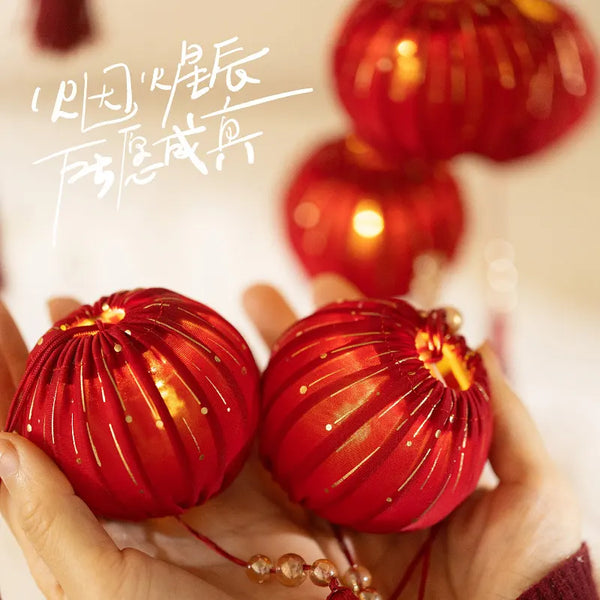 Red decorative Small Festive Red Fabric Lantern with LED Light and Tassels held in hands with blurred red lanterns in the background