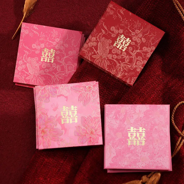 Three small square pink and red Small Gold Foil Double Happiness Wedding Red Envelopes  with gold double-happiness symbols and floral patterns, arranged on a dark red textured fabric background.