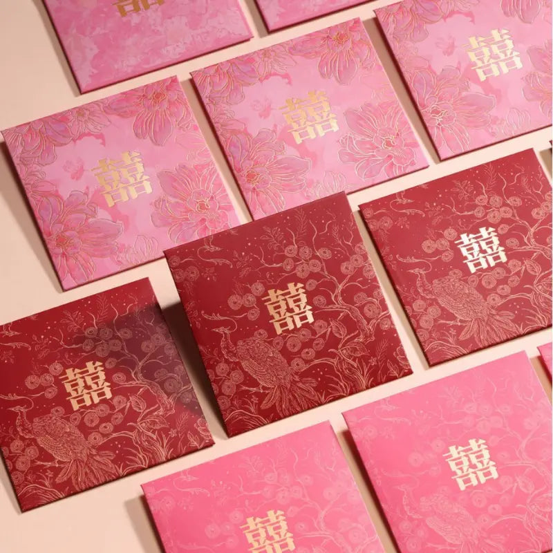 A set of square red and pink envelopes or gift boxes with traditional Chinese double happiness symbols and floral patterns, arranged on a light beige background.