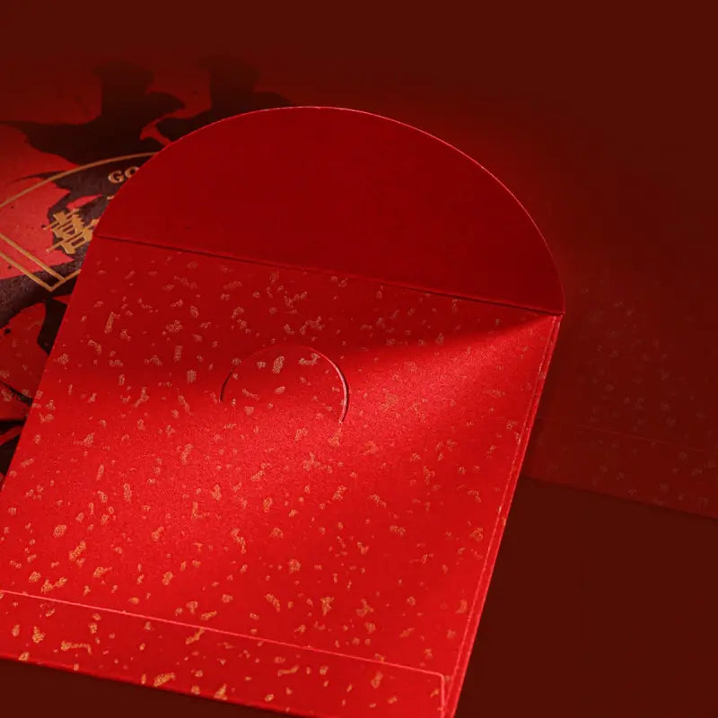 A close-up of a red envelope with a textured, glittery gold speckled pattern, set against a matching dark red background.