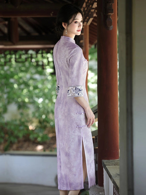 A woman wearing a light purple cheongsam dress with blue and white embroidered sleeve details, standing in a traditional Chinese garden pavilion.