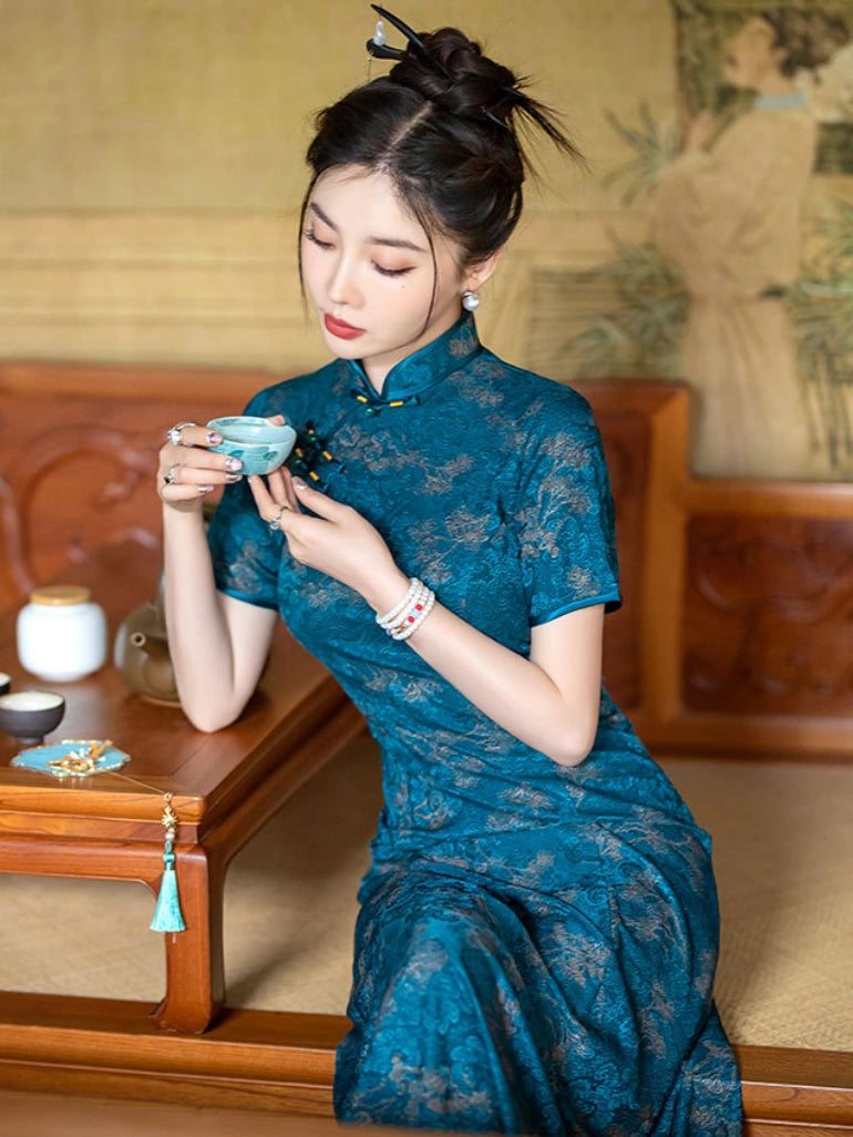 A woman wearing a  Teal Blue 3D Textured Floral Jacquard A-Line cheongsam (qipao) dress sits indoors holding a small light blue teacup. The background features traditional wooden furniture and a warm-toned wall mural.