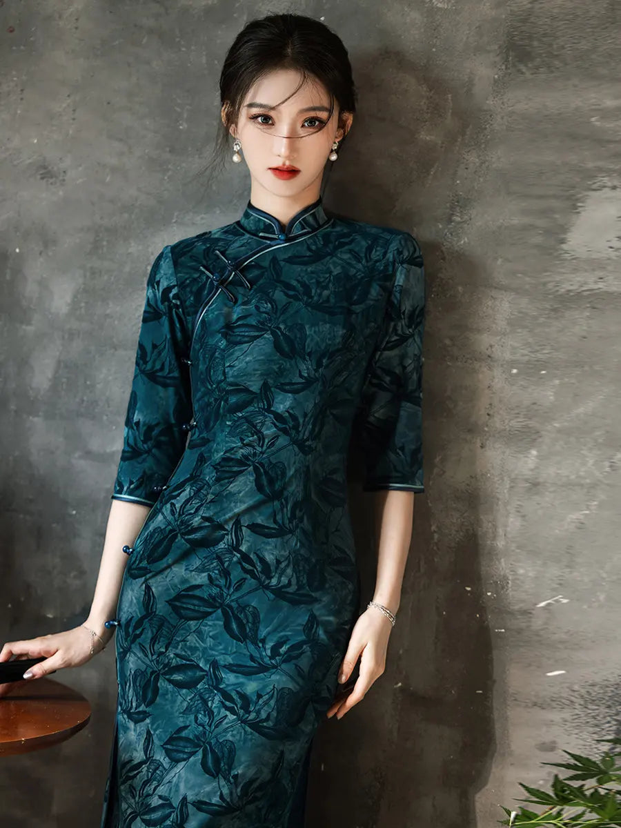 Woman wearing a Teal Foral Velvet Half Sleeves Qipao Cheongsam Dress traditional dress against a gray wall.