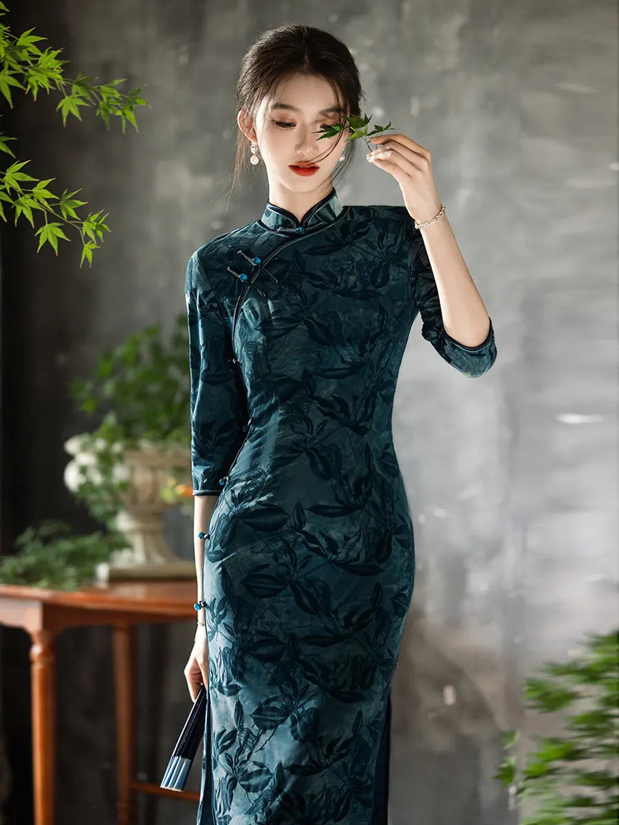 Woman in a Teal Foral Velvet Half Sleeves Qipao Cheongsam traditional dress holding leaves against a gray background