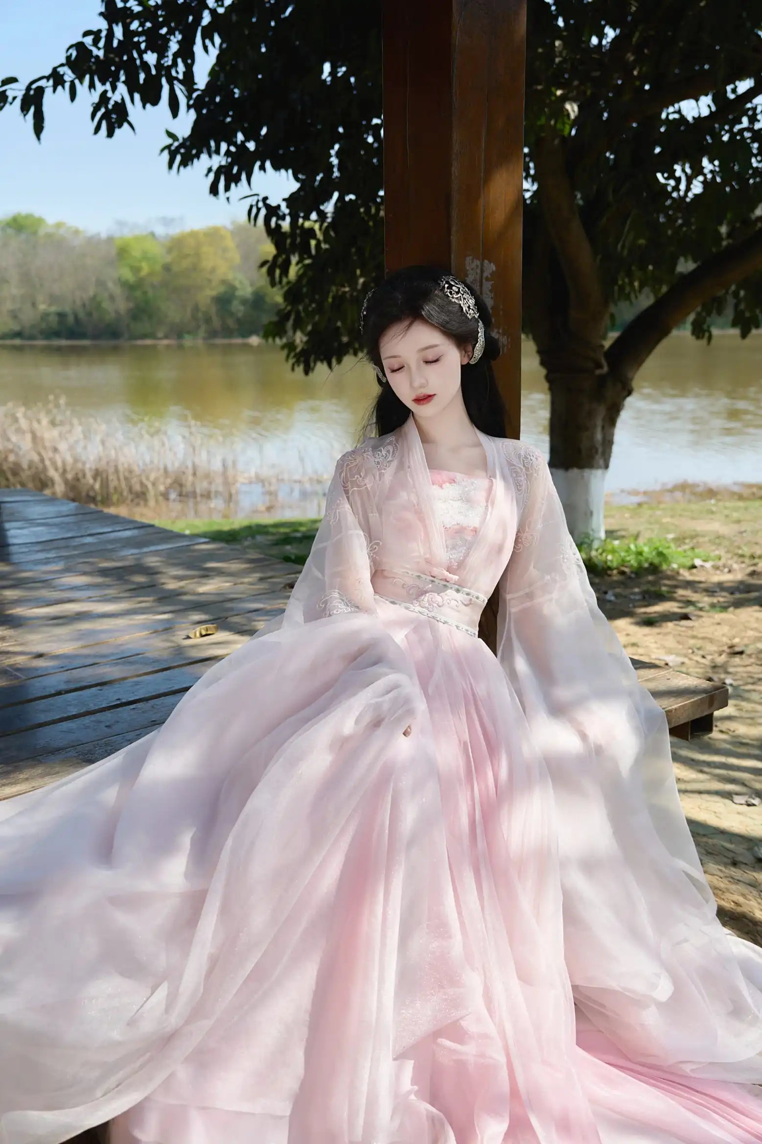 Woman in Traditional Chinese Clothing - Pink Tang Dynasty Hezi Qun Hanfu Dress sitting by a lake with trees in the background