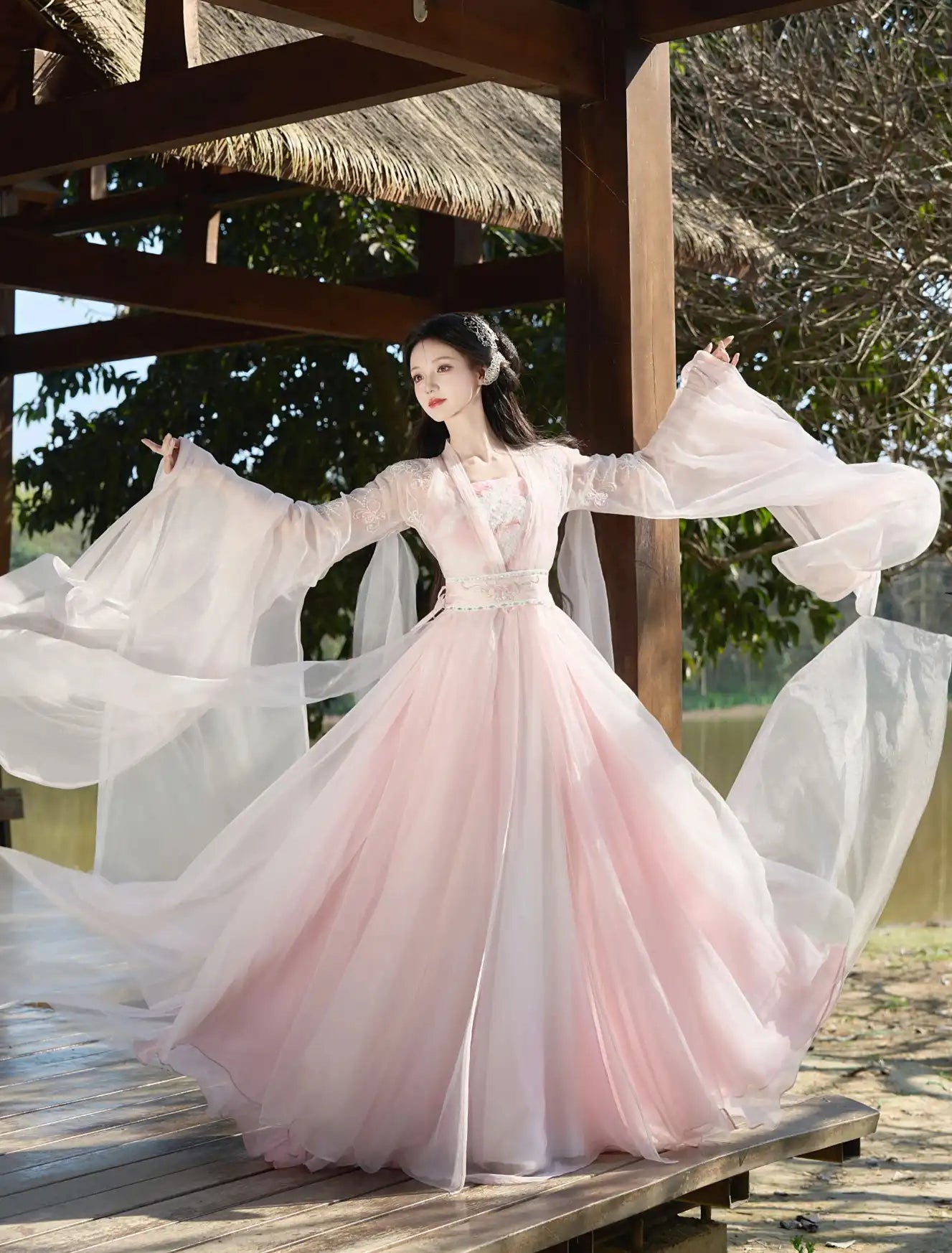 Woman in a flowing Traditional Chinese Clothing - Pink Tang Dynasty Hezi Qun Hanfu Dress standing outdoors under a thatched roof.