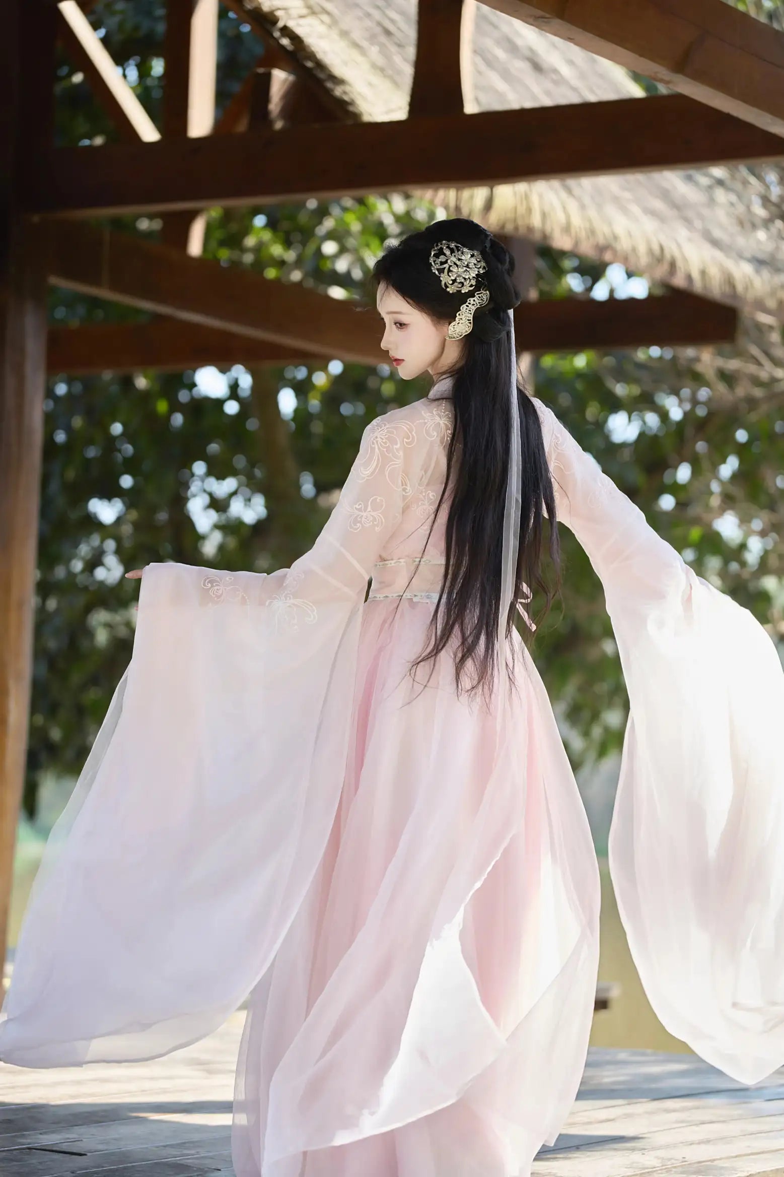 Woman in a Traditional Chinese Clothing - Pink Tang Dynasty Hezi Qun Hanfu Dress with long black hair, standing outdoors under a wooden structure.