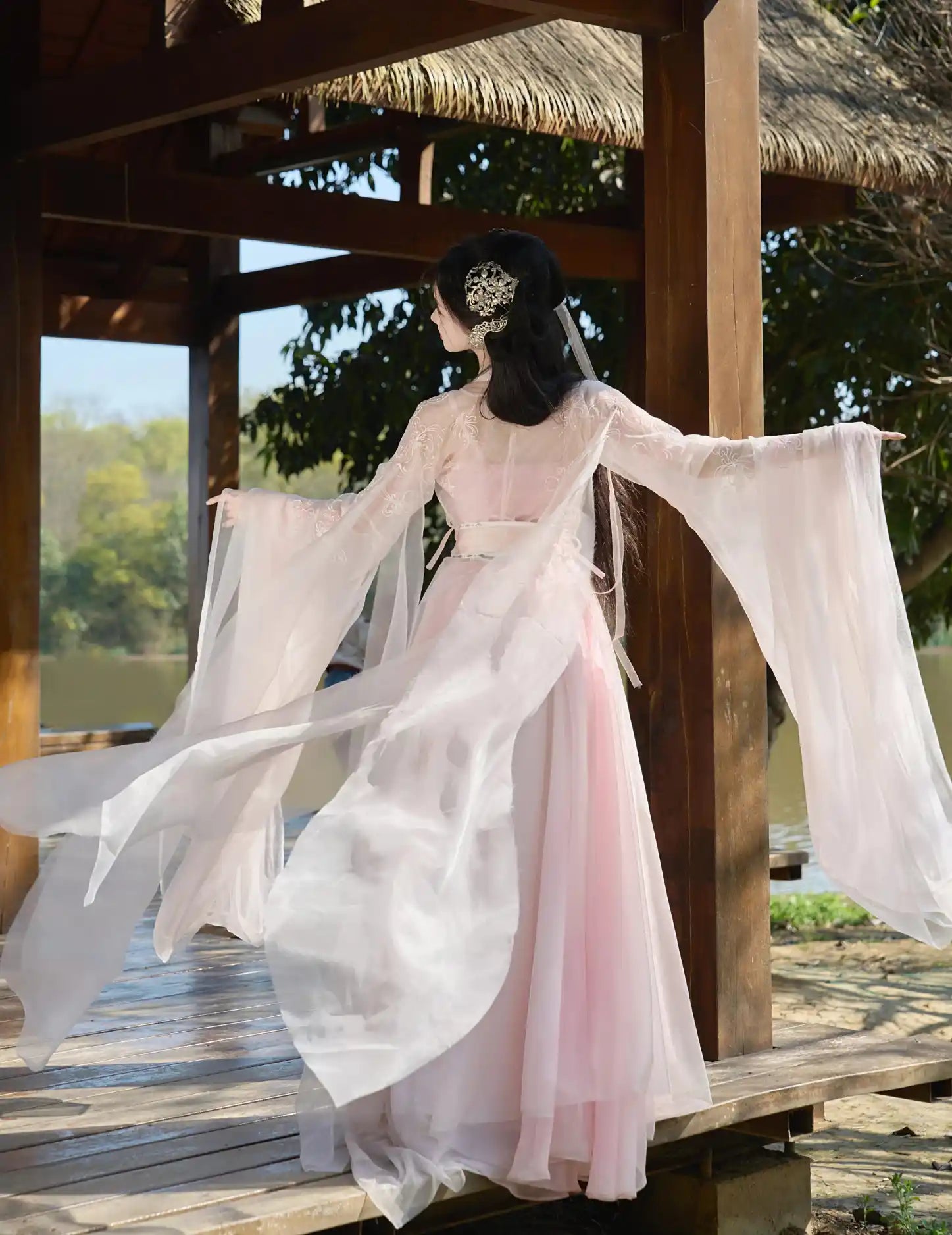 Person wearing a traditional pink and white dress with flowing sleeves in a natural setting.