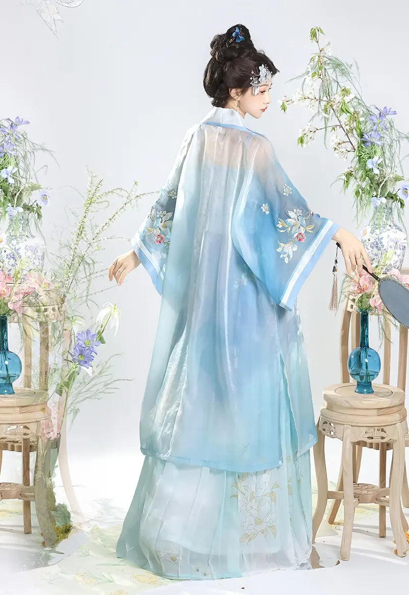 Person wearing a  light blue and white Traditional Chinese Dress – Elegant Song Dynasty Hanfu Set  with floral embroidery, standing in a decorative setting with flowers and chairs.