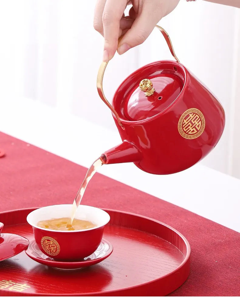 Traditional Chinese Red  Double Happiness Wedding Tea pot with gold accents pouring tea into a matching red cup on a red tray.