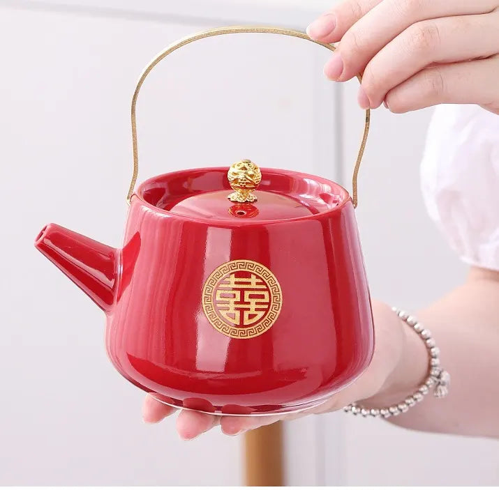 Red teapot with gold double happiness chinese charactor  held by a hand on a white background