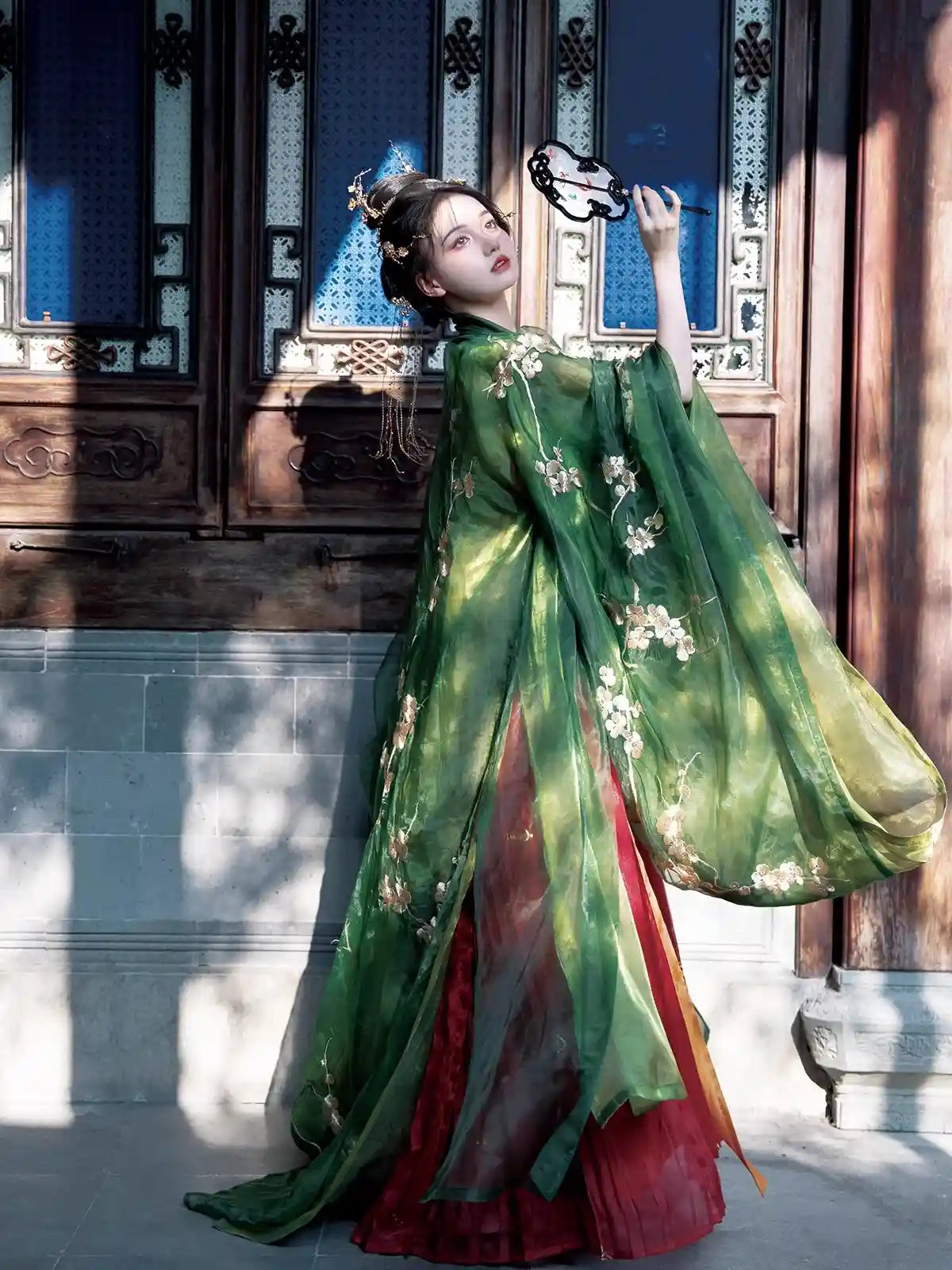 Woman in a traditional green and red dress Traditional Chinese Tang Dynasty Green Hanfu Dress with floral patterns standing in front of wooden architectural elements.