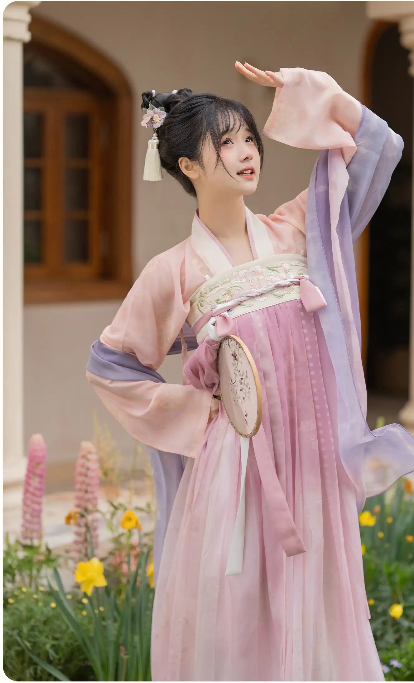 Woman in Traditional Chinese Tang Dynasty Pink Hanfu Dress Clothing  standing outdoors with flowers and a building in the background