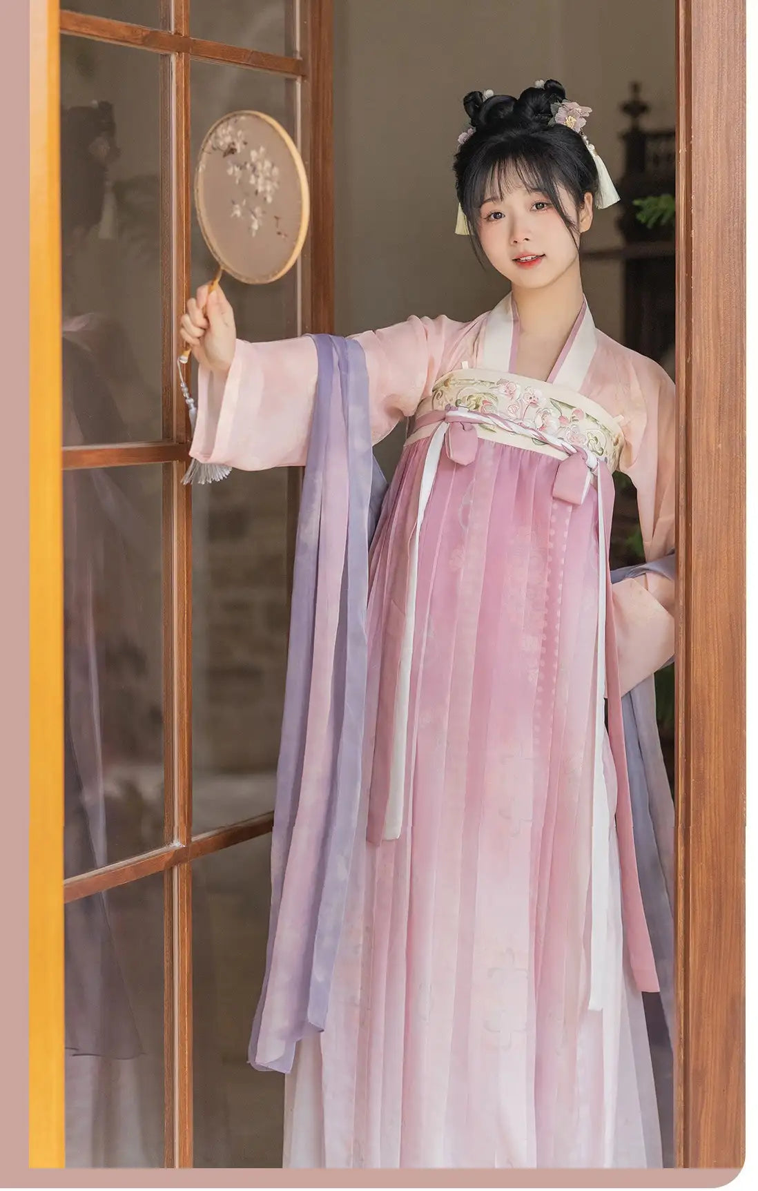 Woman inTraditional Chinese Tang Dynasty Pink Hanfu Dress Clothing e holding a fan, standing in front of a wooden door.