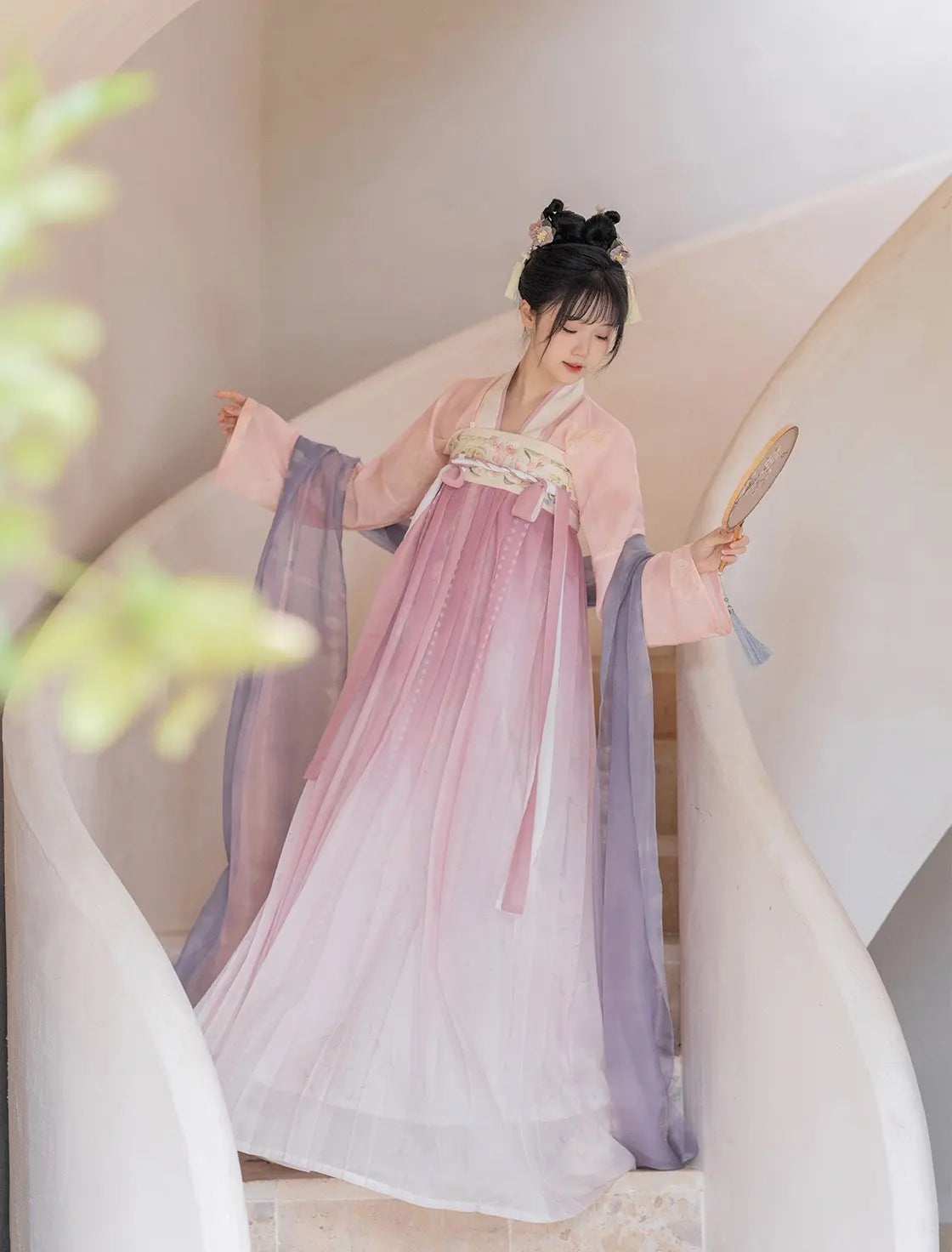 Woman in traditional Hanfu dress holding a fan against a neutral background