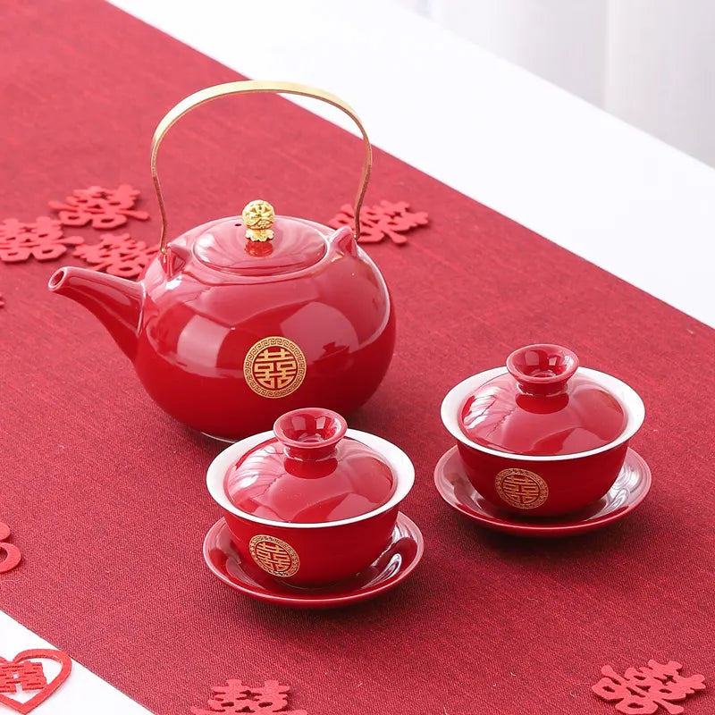 Red teapot and two teacups with gold double happiness  on a red tablecloth.