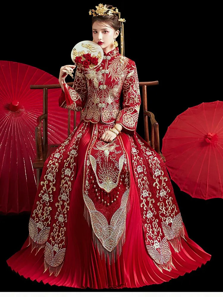 A woman wearing an ornate red and gold traditional Chinese wedding gown sits on a wooden chair against a black background, holding a red fan. Red paper umbrellas are visible on both sides.
