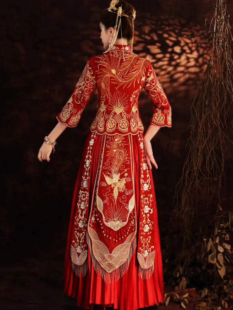 A woman shown from the back wearing a traditional Chinese red and gold embroidered qun kwa wedding dress with three-quarter sleeves and a long pleated skirt, posed against a dark, atmospheric background with warm lighting.
