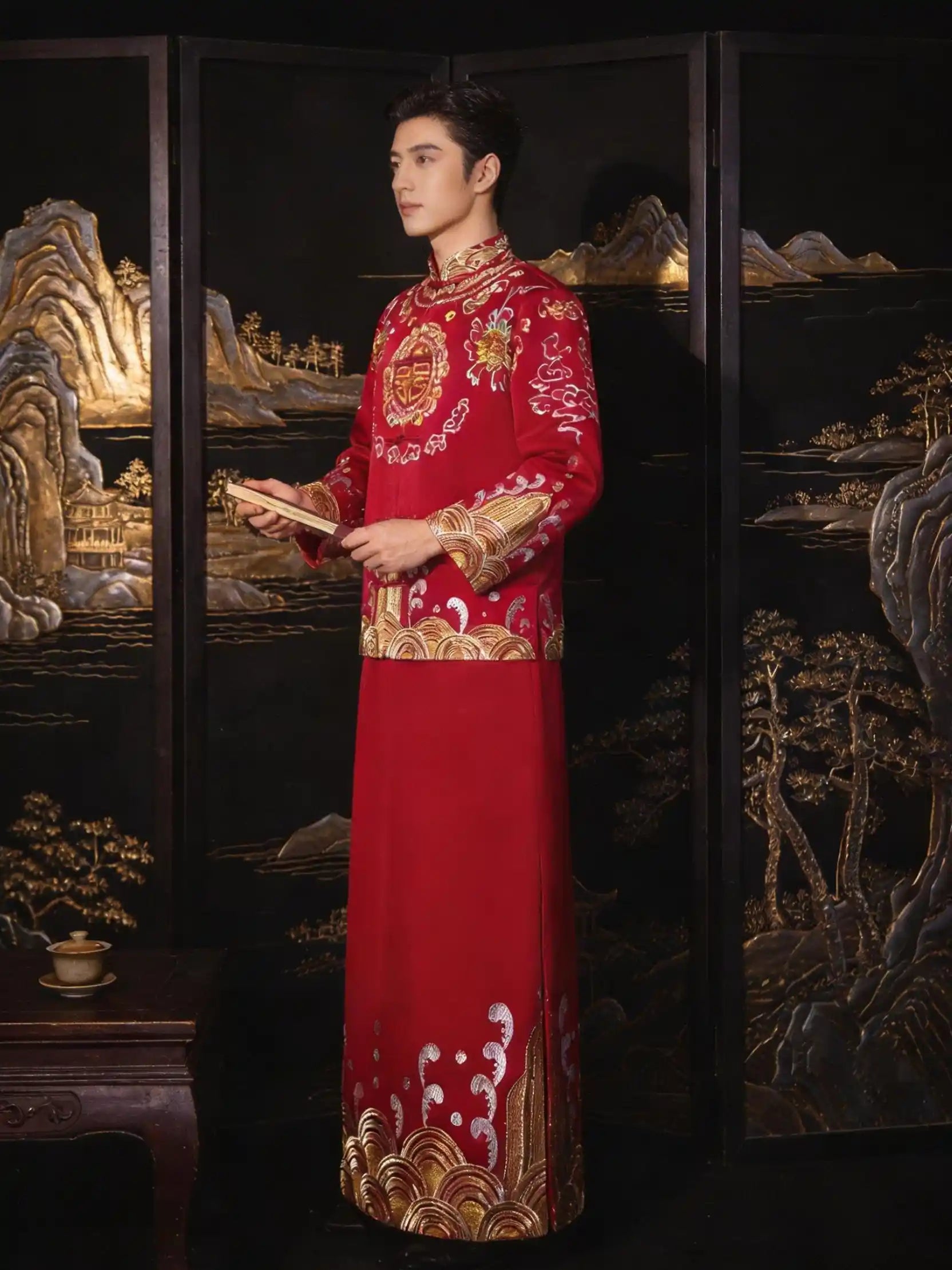 Person wearing a tTraditional Red and Gold Double happiness Groom's Tang Suit Gown  with intricate patterns against a decorative background.