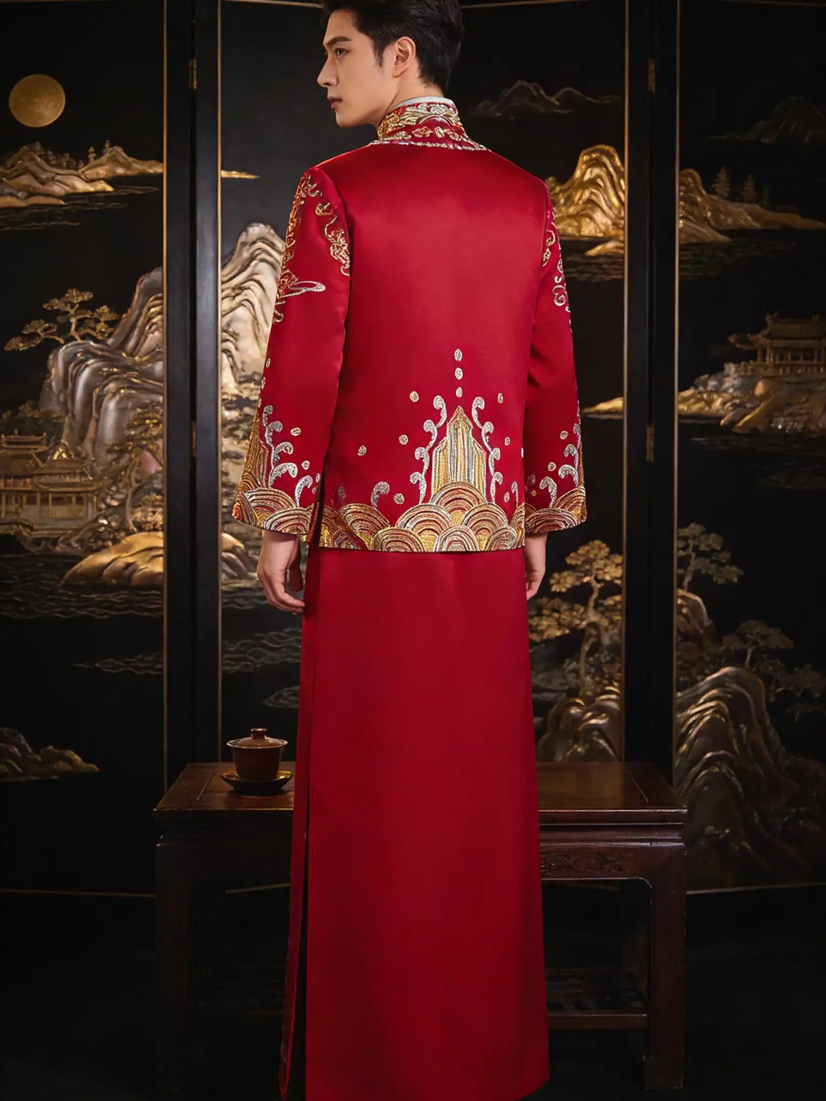 Person wearing a Traditional Red and Gold Double happiness Groom's Tang Suit Gown embroidered outfit in front of an ornate black and gold background.