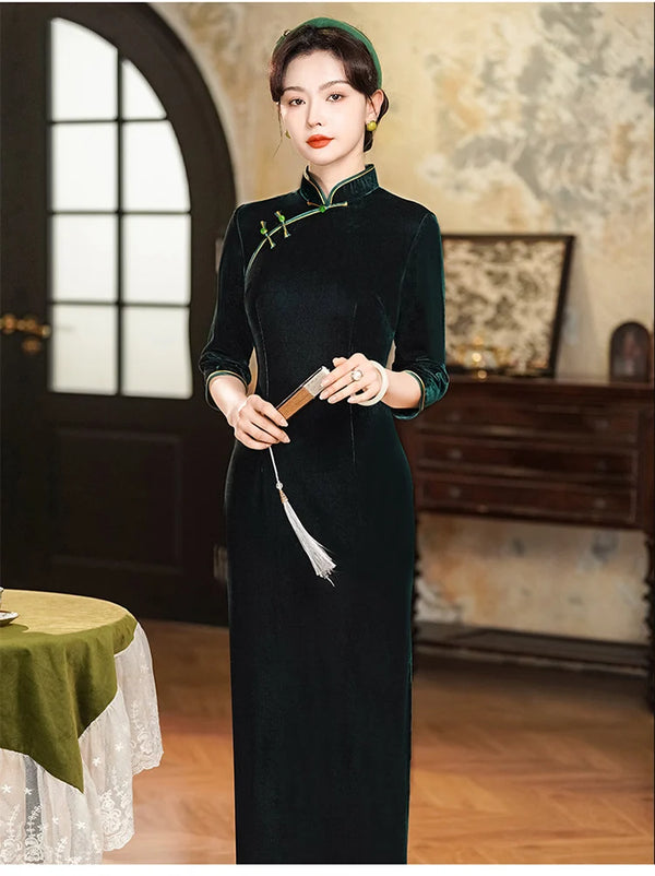 Woman in a long Vintage Emerald Green Velvet Long Sleeves Qipao Dress holding a fan in an elegant room.