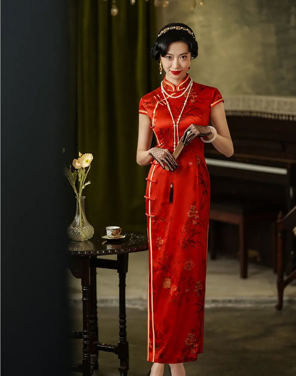 Woman in a Vintage Foral Red Silk Qipao Cheongsam Dress holding a brush in a room with dark walls and a piano.