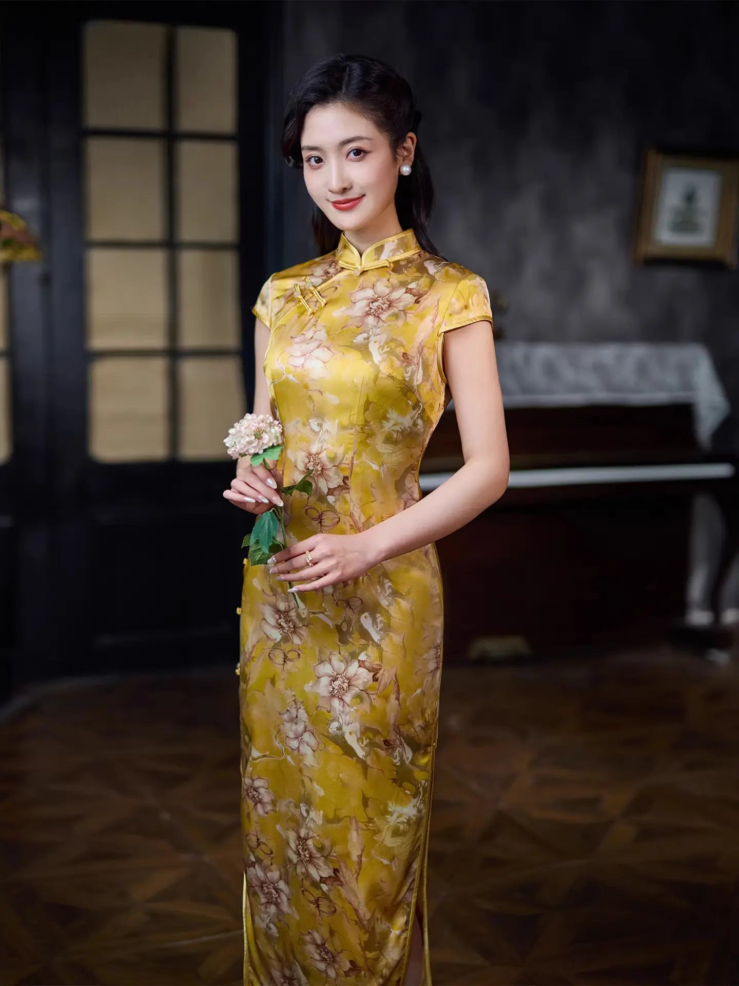 Woman in a yellow Vintage Gold Mulberry Silk floral  Chinese Long Qipao dress standing in a room with a dark background